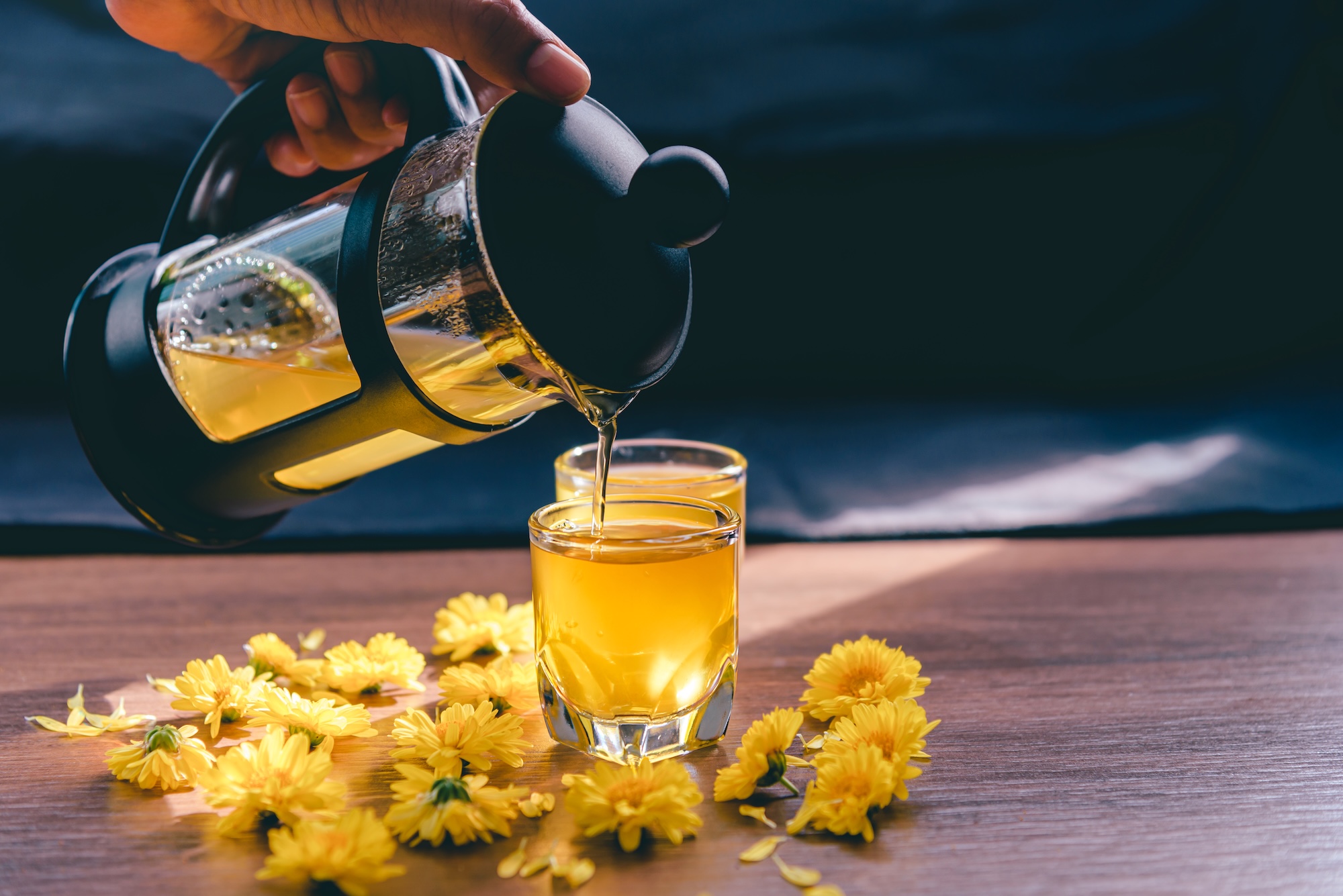 Chrysanthemum tea in glass on wooden table and flowers with sun light and black background,Healthy beverage,juice for drink,Help reduce blood pressure,prevent heart disease, Herbs and medical concept.